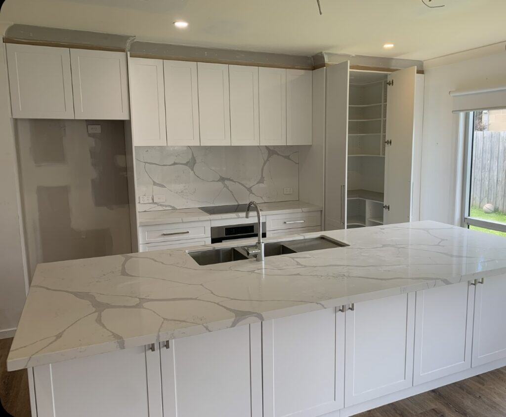 kitchen renovations all white cabinetry, with sink and oven/stove top installed. storage underneath the kitchen bench.